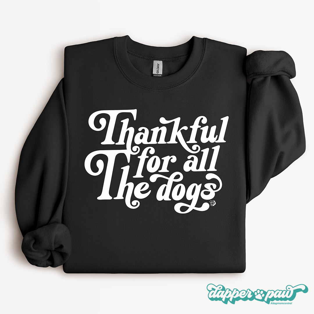 A black crewneck sweatshirt with the phrase 'Thankful for all The dogs' printed in a white retro-style script across the chest.