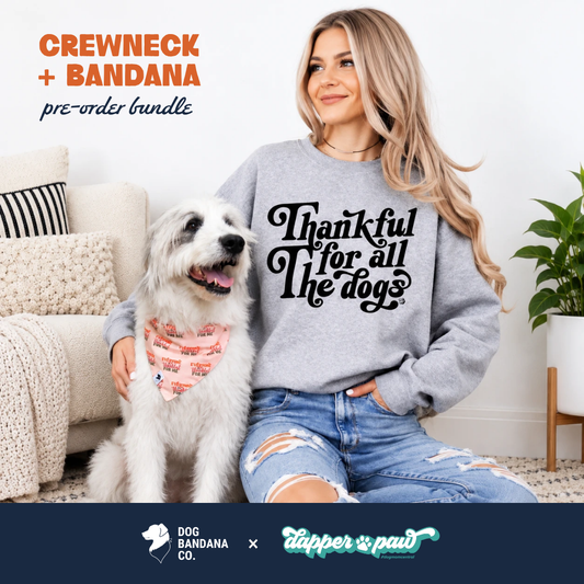 Woman in a gray "Thankful For All The Dogs" crewneck sitting with a fluffy white dog wearing the Dog Bandana Co. "Everyone Is Thankful" reversible Thanksgiving bandana